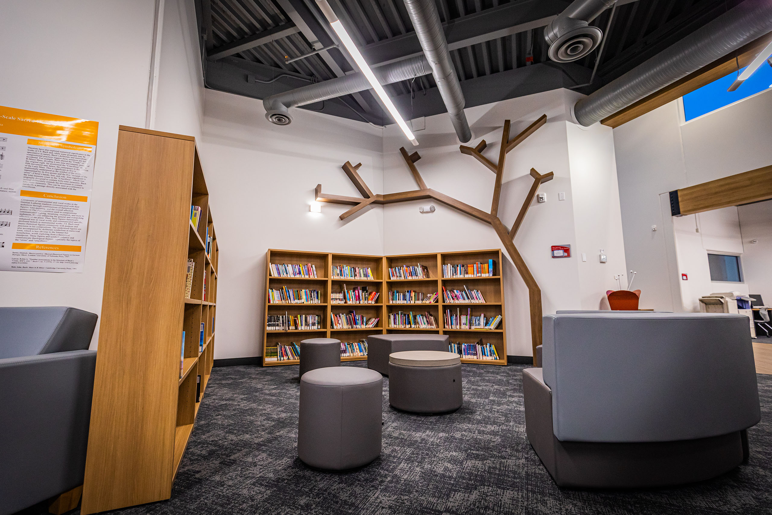 Seating area within a library containing wood installations, shelves with books, abstract carpet flooring and grey seats