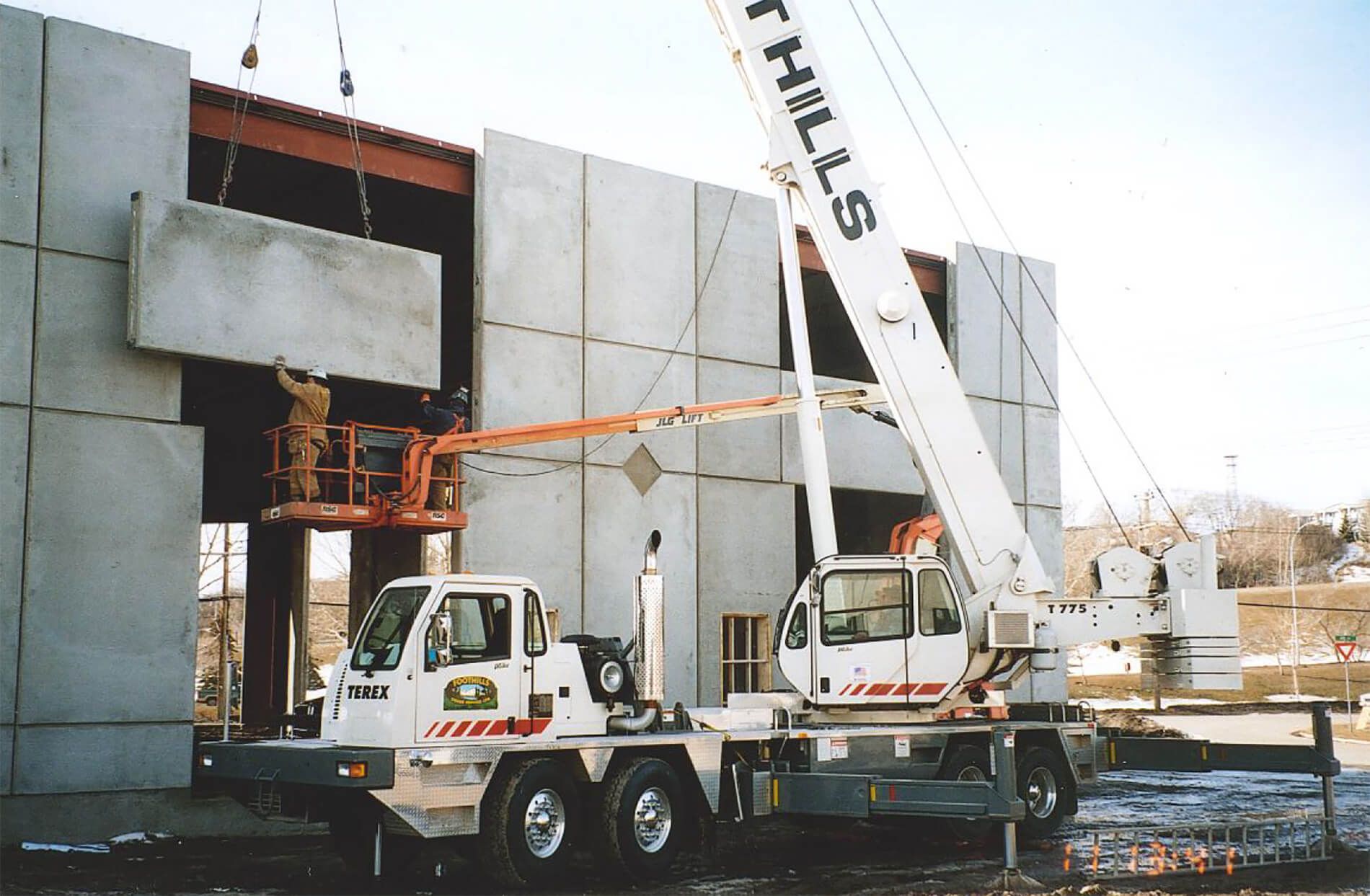 A crane, along with two employees, inserting a concrete panel into place