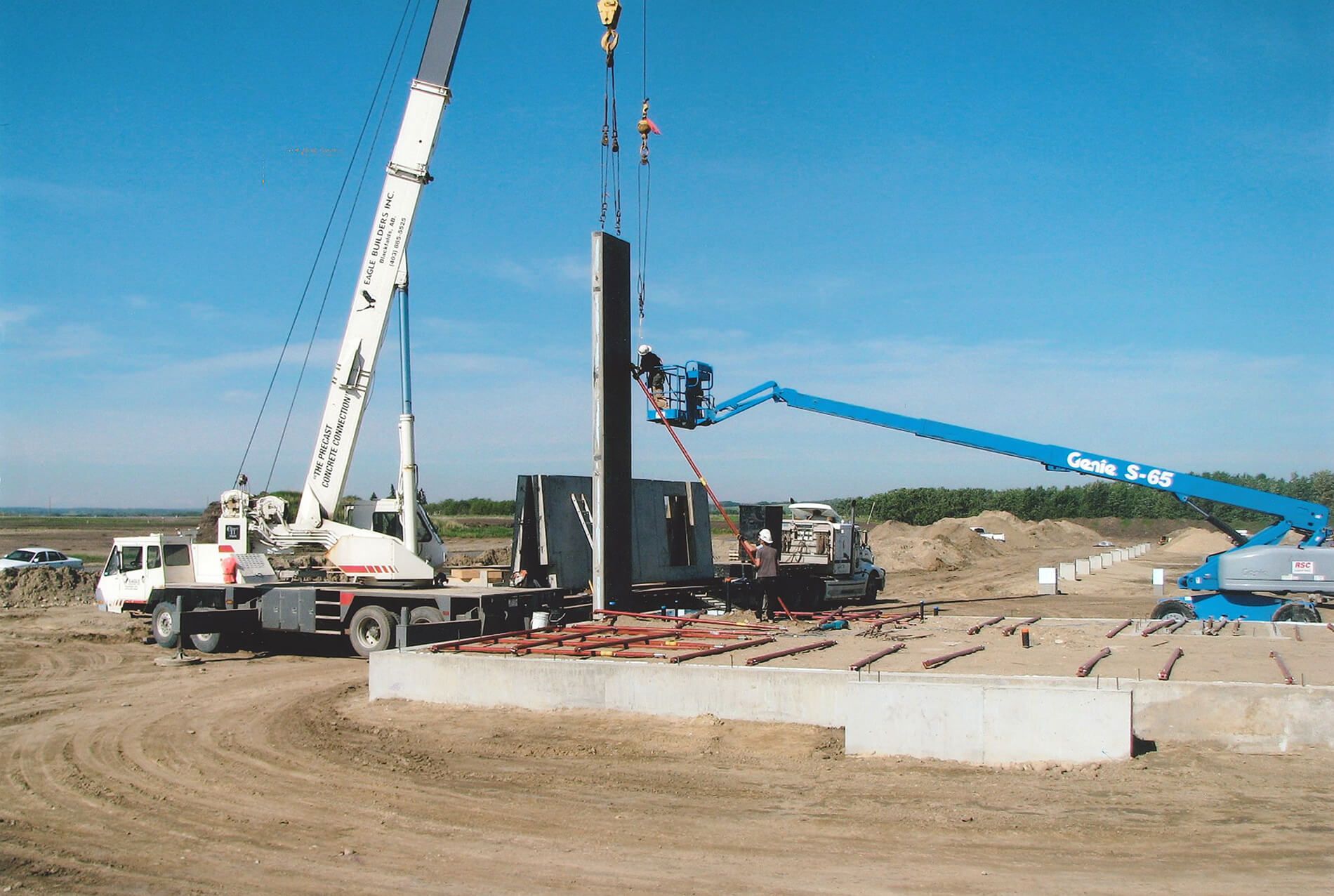 Two cranes inserting a concrete panel into place