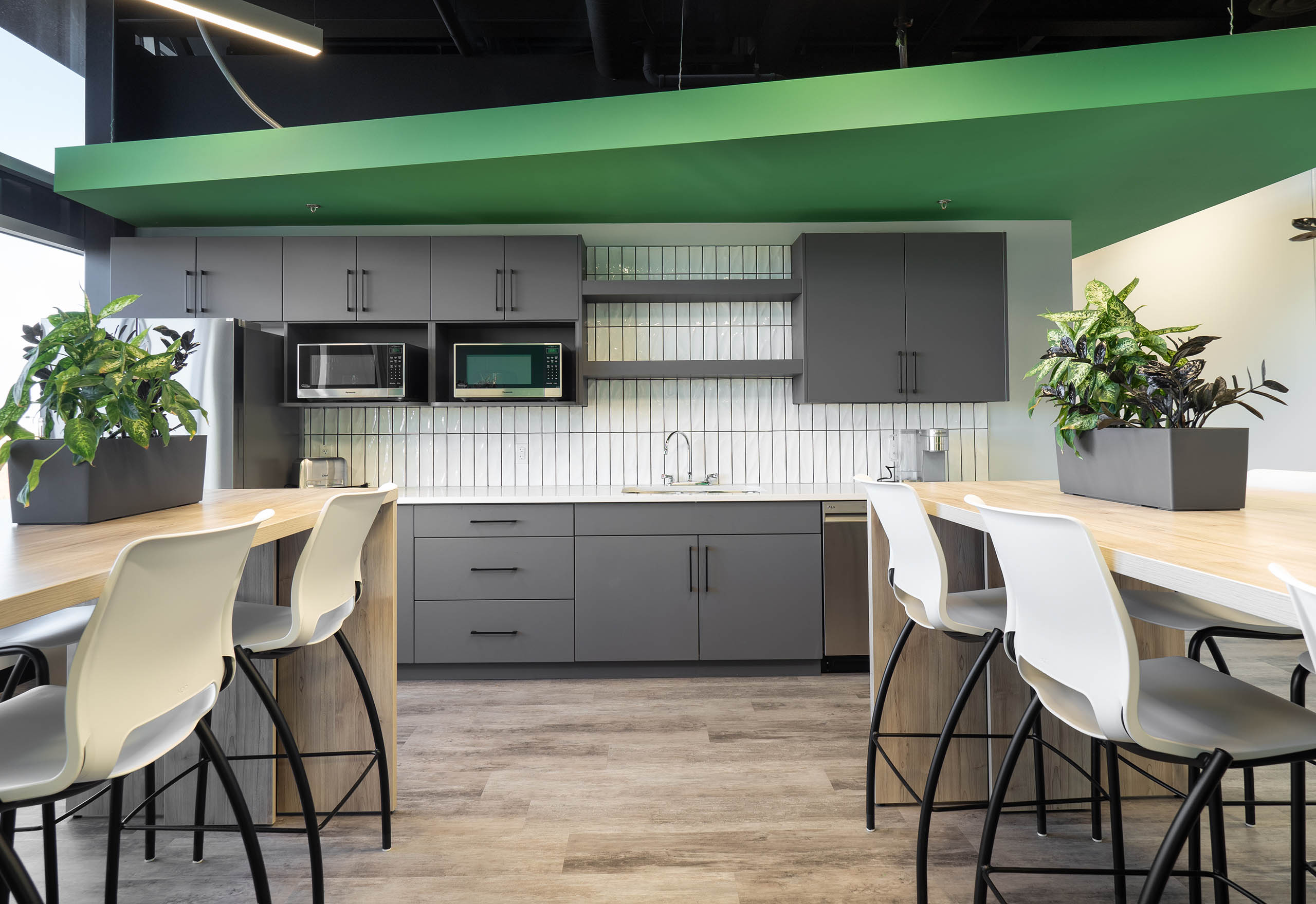 Kitchen and dining area with wood flooring and tables, grey and green walls, along with white stool chairs