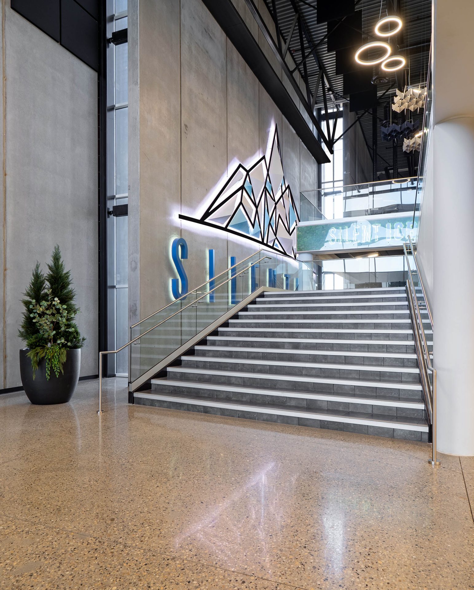 View of a staircase with an LED sign of the Silent Ice logo placed on a concrete wall