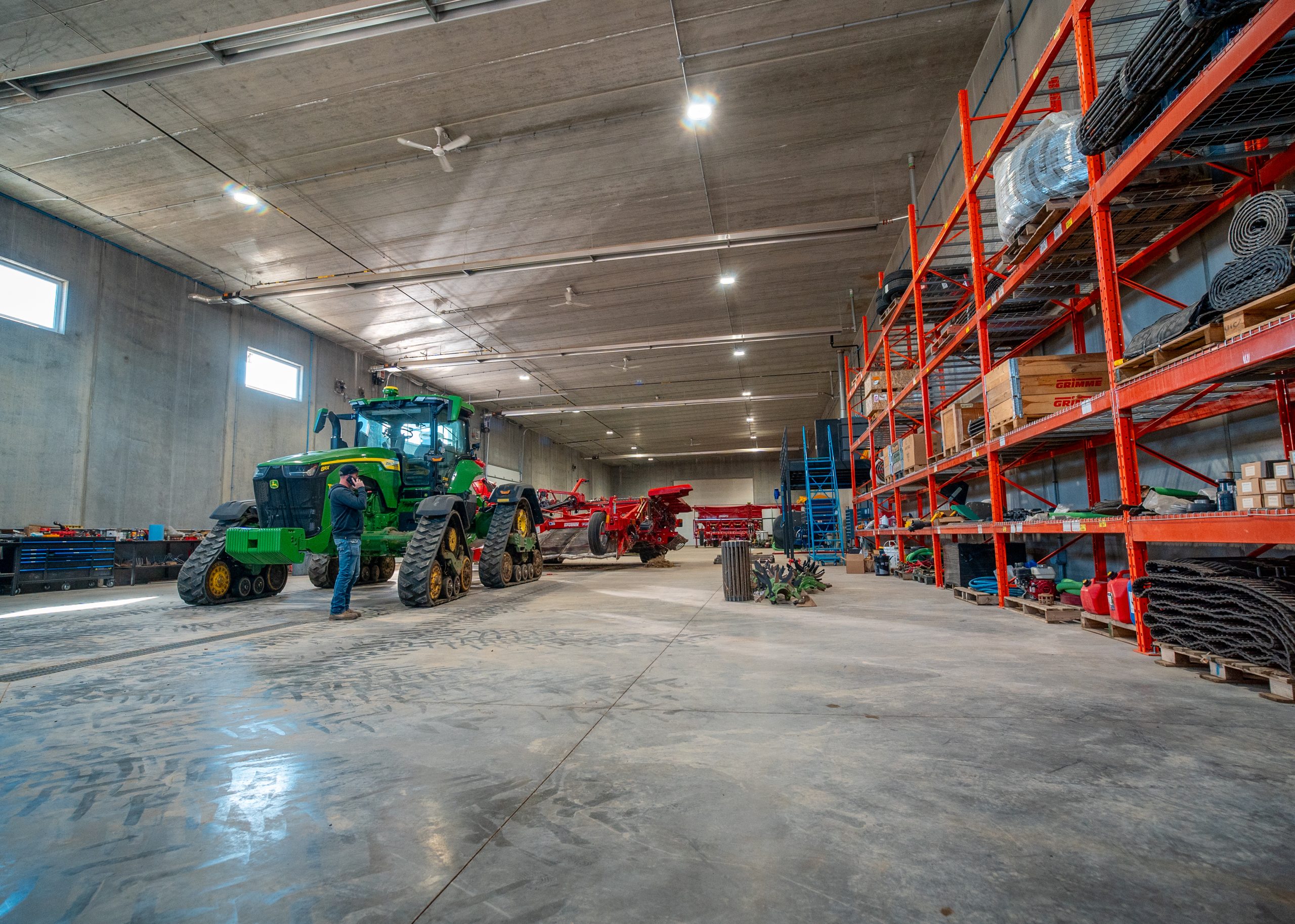 A garage and storage area with concrete flooring and a gentleman on the phone standing in front of a green tractor
